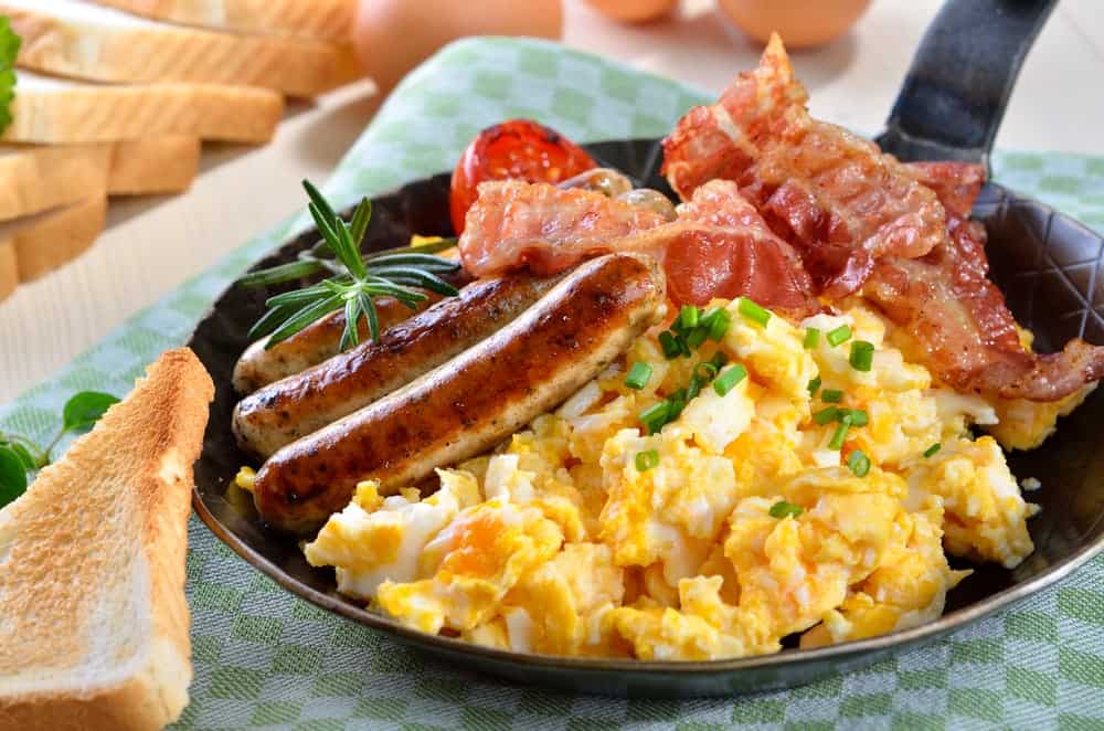 A skillet with scrambled eggs, bacon, and sausage.
